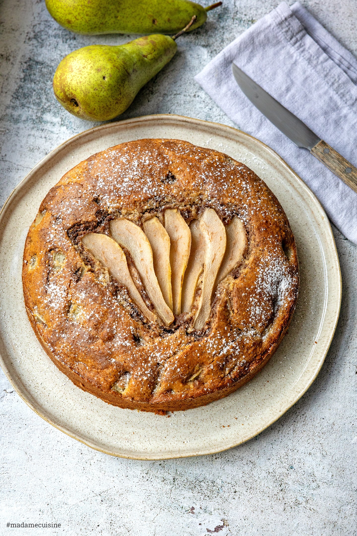 Birnen-Nuss-Kuchen von oben mit Birnenspalten und Puderzucker auf beigem Teller