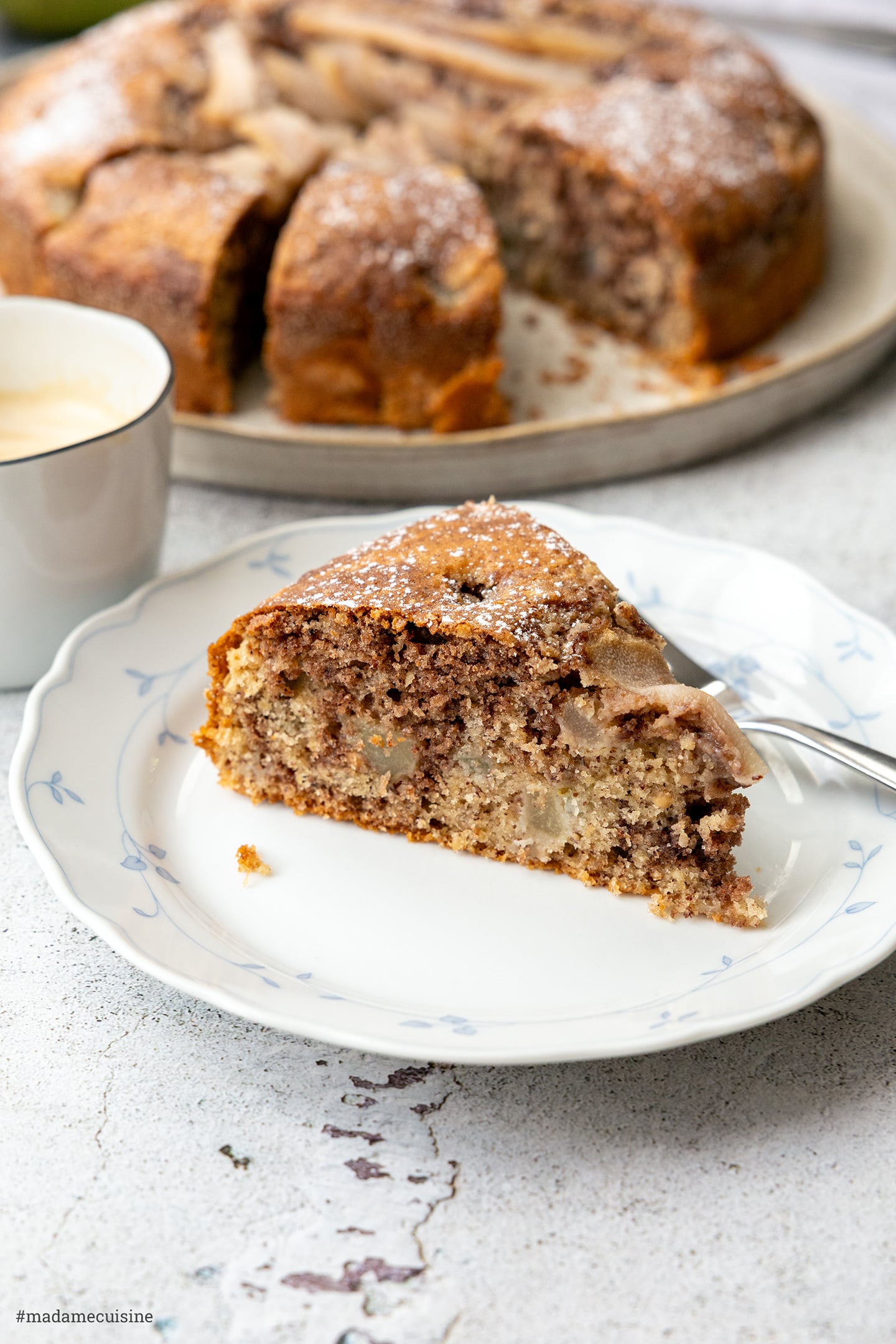 Birnen-Nuss-Kuchen mit Milchkaffee, Kuchenstück auf Teller vor dem ganzen Kuchen