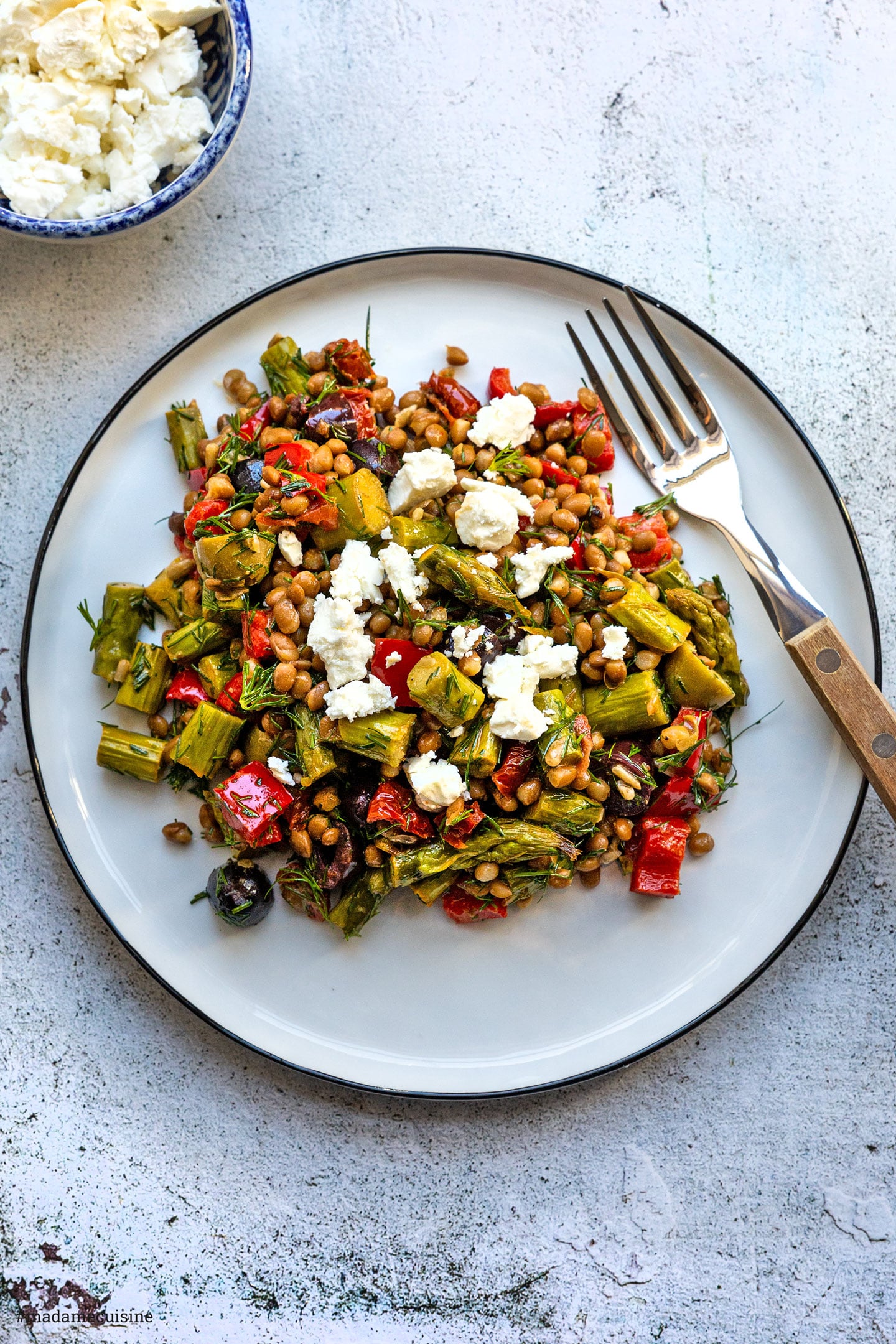 Linsensalat mit grünem Spargel und zerbröckeltem Feta auf weißem Teller