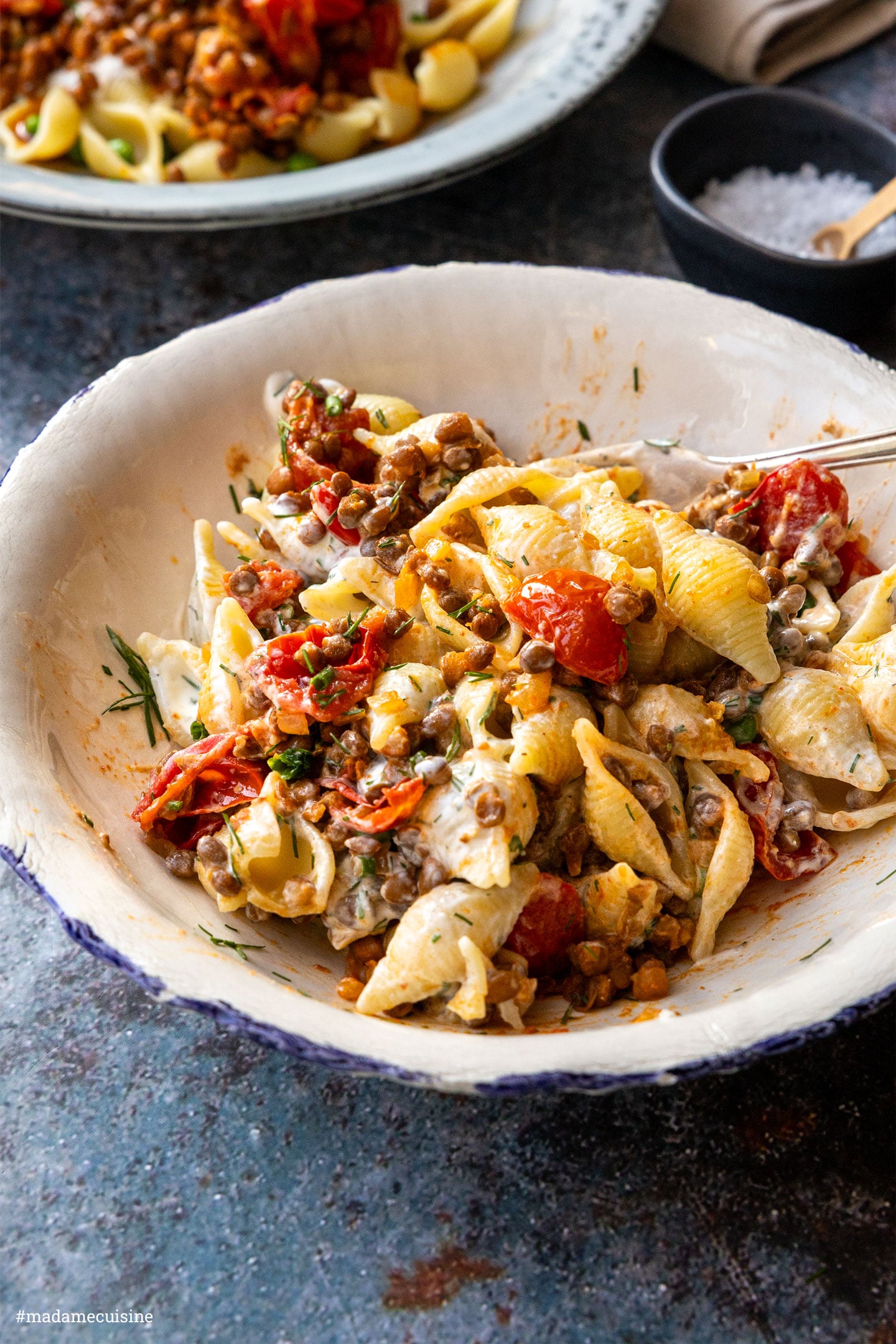 Nahaufnahme türkische Pasta mit Linsen: Muschelnudeln mit gebratenen Kirschtomaten, Linsen und Joghurt-Sauce in einer weißen Schüssel – im Hintergrund ein zweiter Teller mit Erbsen