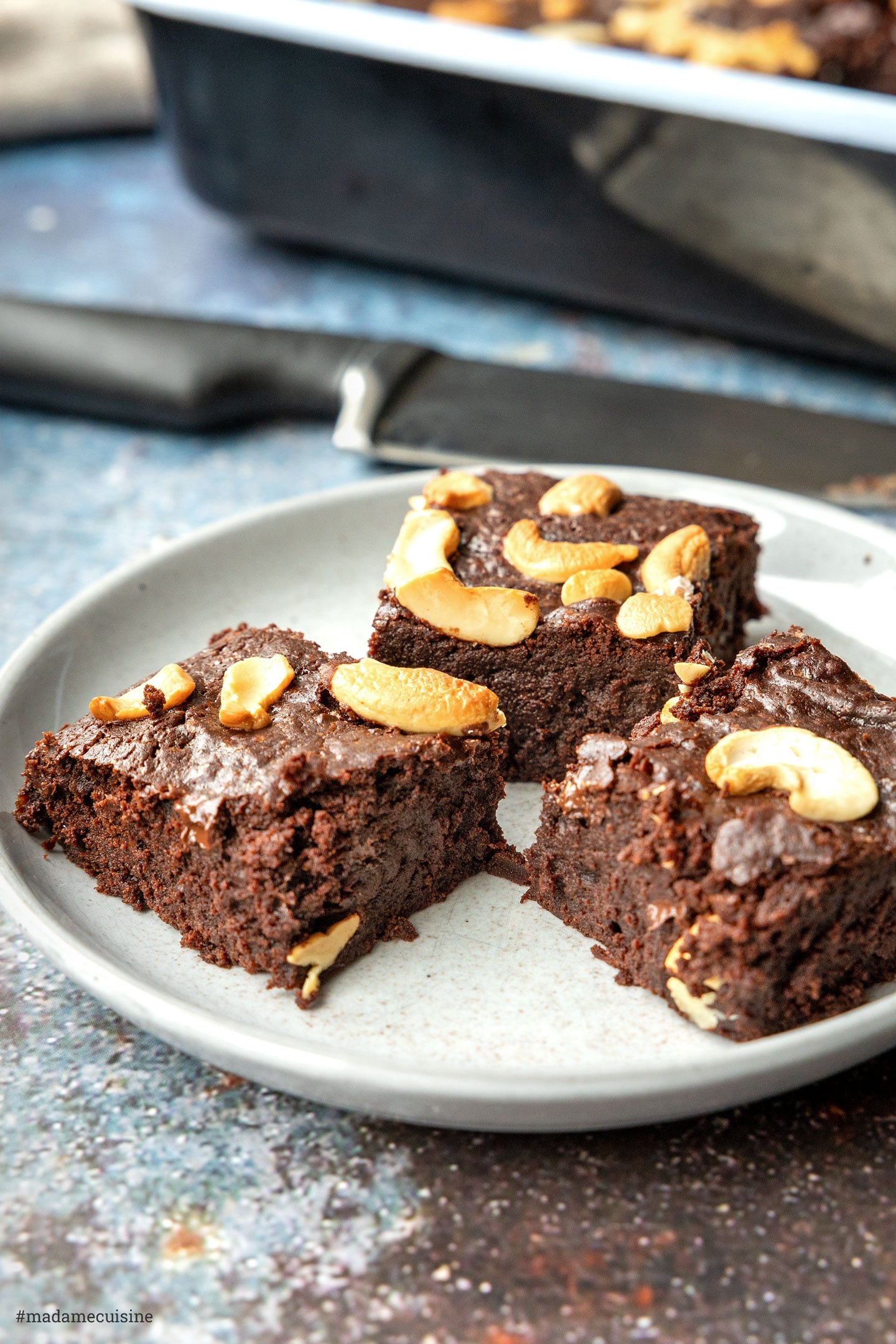 Drei Stücke vegane Brownies mit Cashewnüssen auf grauem Teller