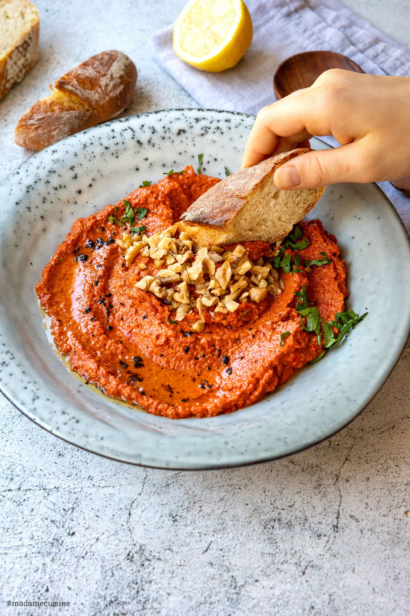Hand tunkt Baguettescheibe in cremigen Paprika-Walnuss-Dip