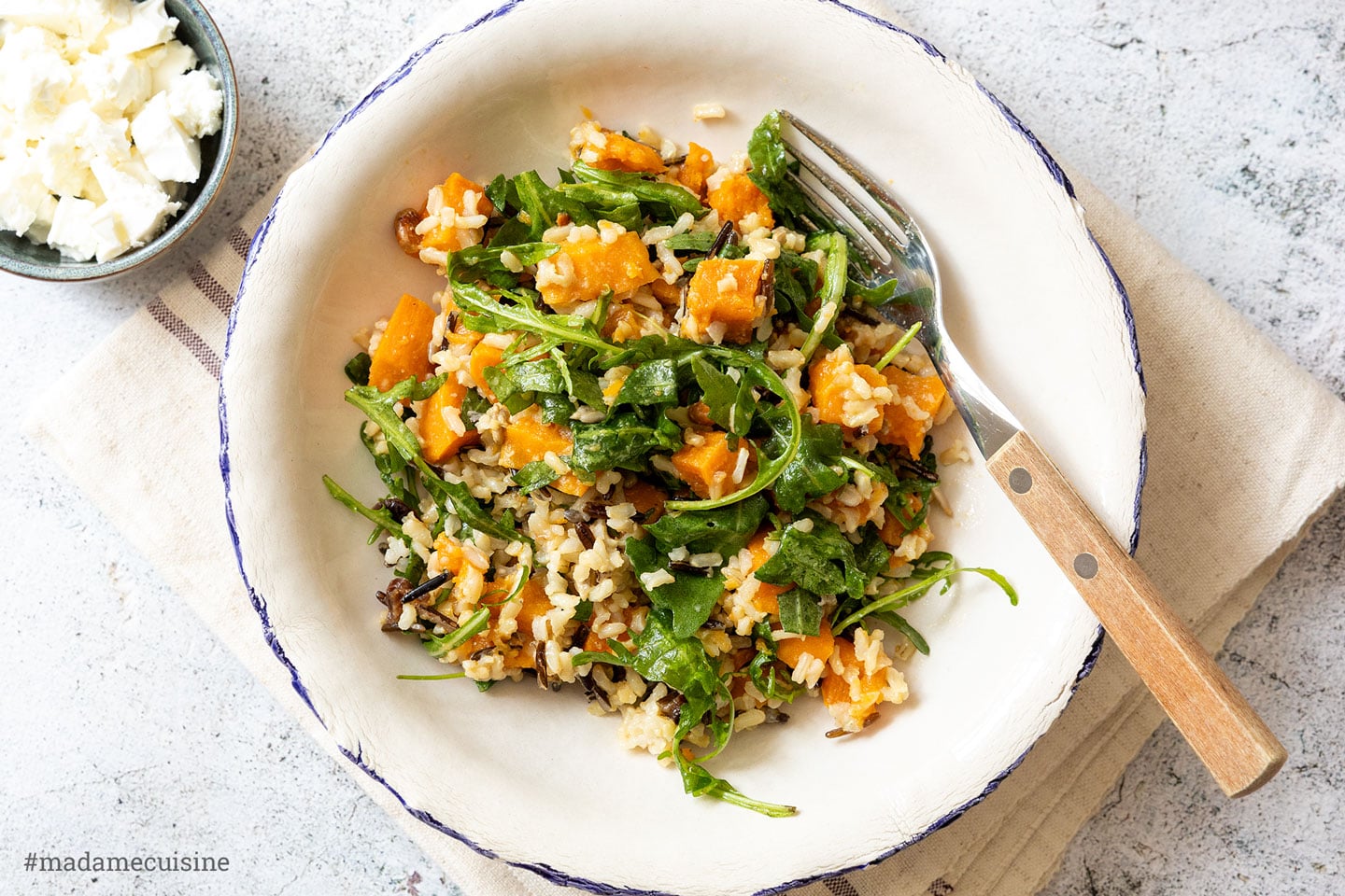 Wildreis-Süßkartoffel-Salat mit Rucola und Feta in einem weißen Teller mit blauem Rand