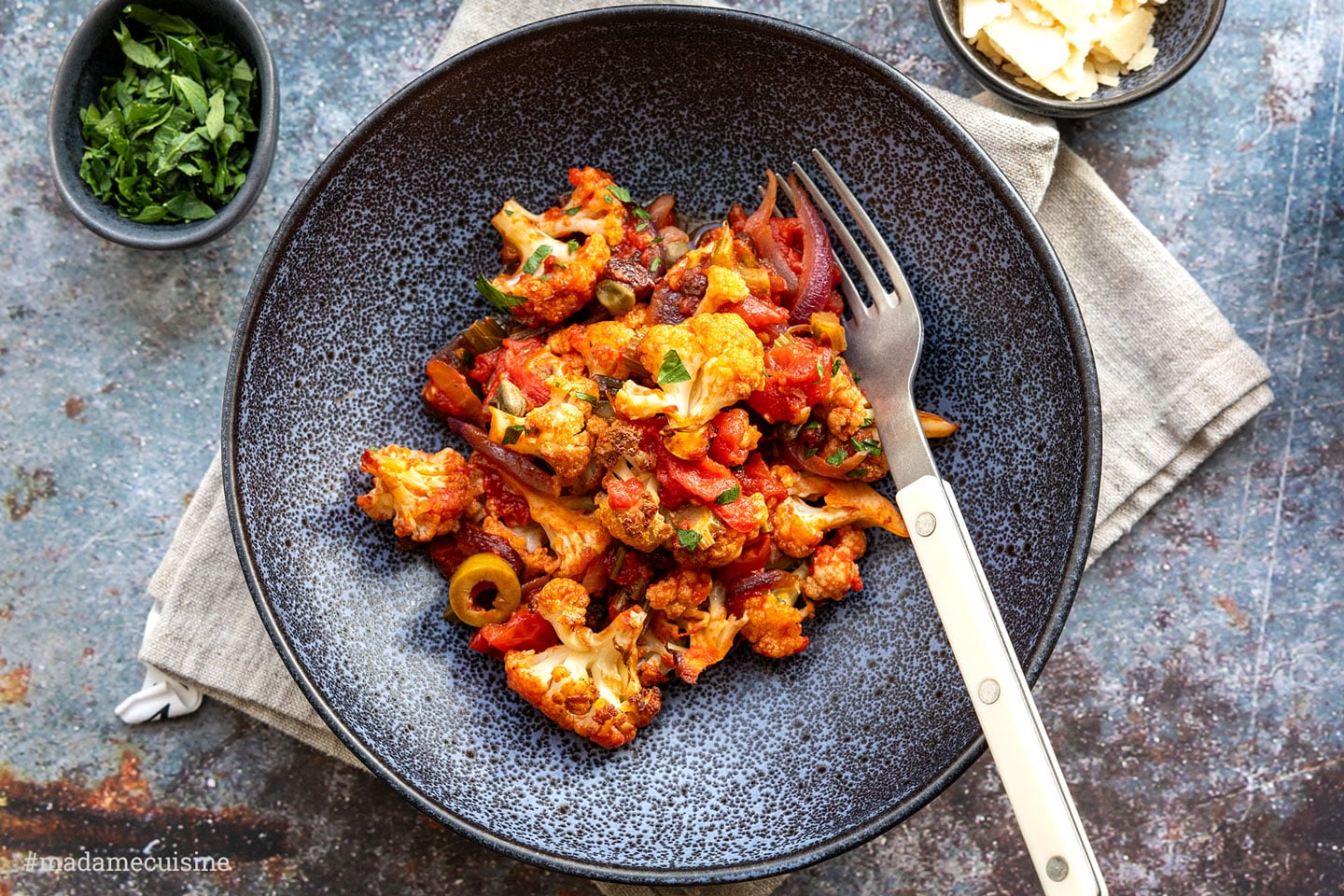 Blumenkohl-Caponata auf dunklem Teller mit Selleriegrün und Parmesan