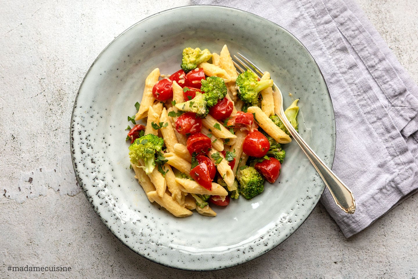 Hummus-Pasta mit Brokkoli und Kirschtomaten auf grauem Teller