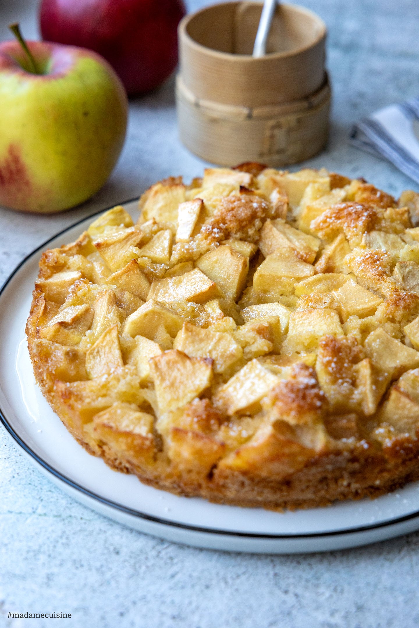 Kleiner Apfelkuchen mit Äpfeln und Puderzucker-Sieb im Hintergrund