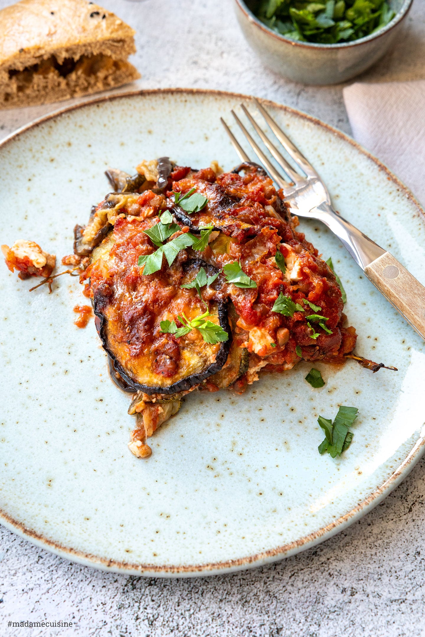 Serviertes Stück Moussaka mit Gabel, garniert mit Petersilie