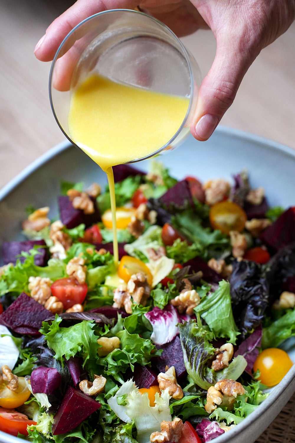Salatdressing über einen gemischten Salat mit Tomaten und Walnüssen gießen