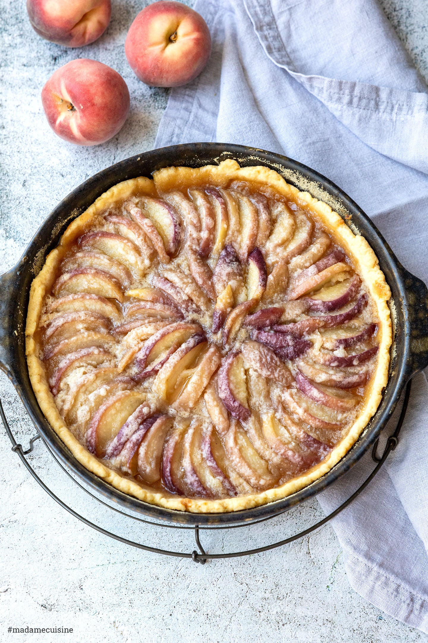 Frisch gebackene Tarte mit dicht überlappenden Pfirsichspalten auf einem Kuchengitter