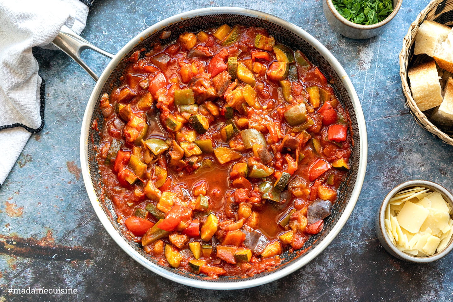 Pisto, spanische Gemüsepfanne mit Aubergine, Zucchini, Paprika und Tomaten in der Pfanne, serviert mit Brot und Manchego
