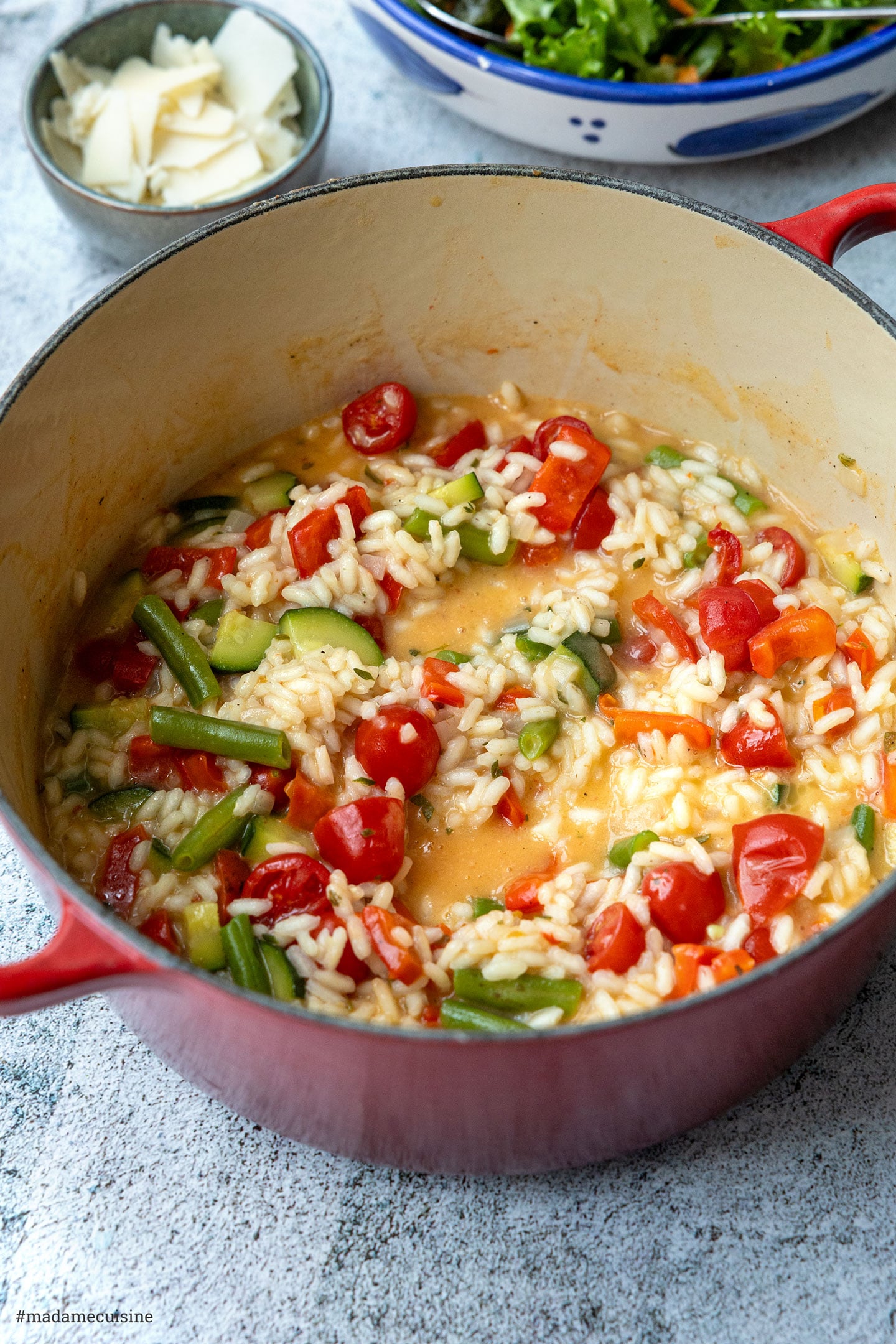 Nahaufnahme von Gemüserisotto im Topf mit bunten Tomaten, Paprikawürfeln und Zucchini