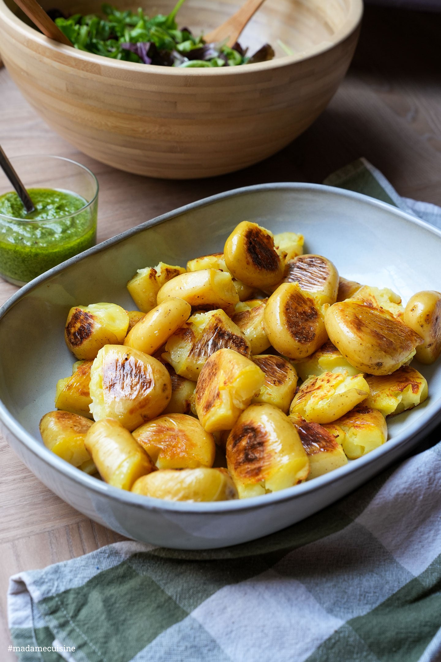 Goldbraun gebratene Kartoffeln in einer Schüssel, daneben Salat und ein kariertes Küchentuch