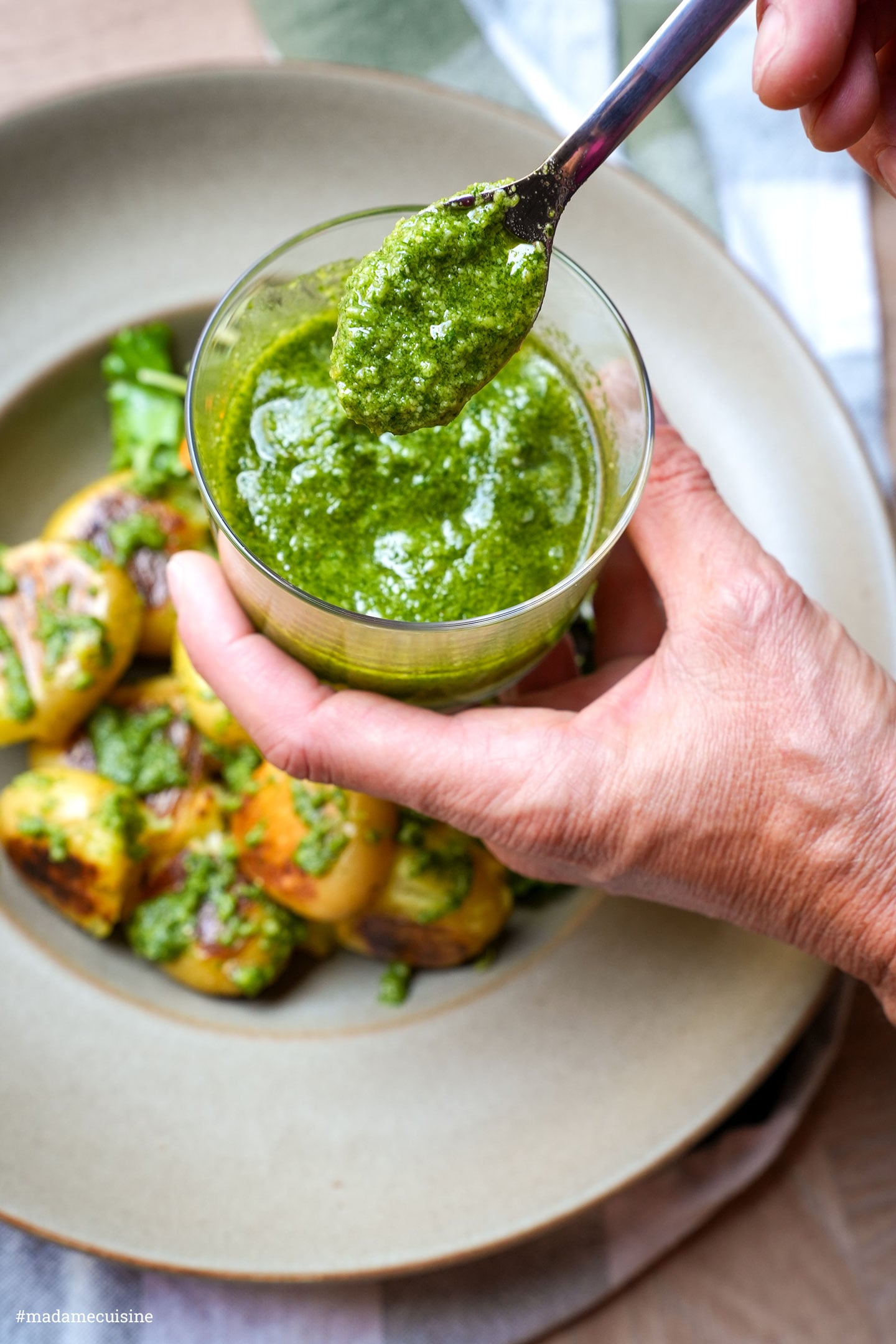 Ein Löffel mit selbstgemachtem Basilikumpesto wird über die Kartoffeln gegeben