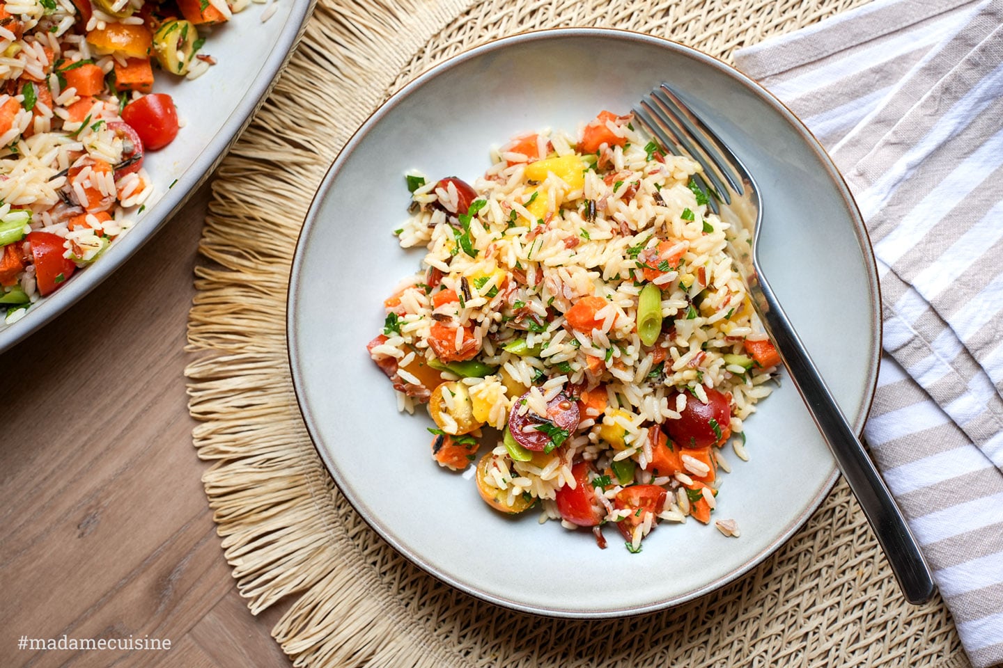 Wildreissalat mit Mango und Süßkartoffel auf Teller angerichtet, mit Gabel und Schüssel im Hintergrund