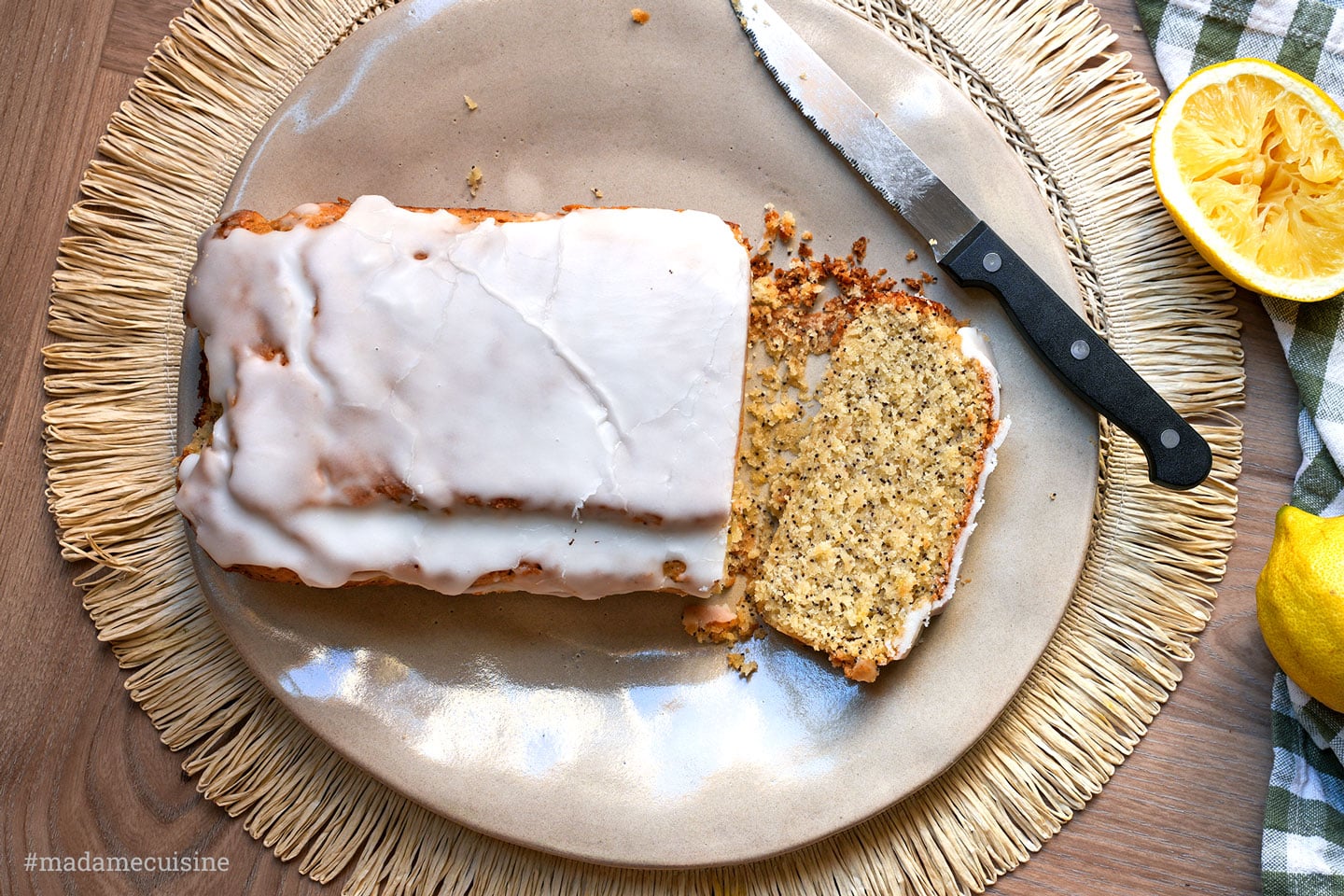 Veganer Zitronenkuchen mit Mohn, angeschnitten auf einem Teller mit Messer und Zitronenhälfte