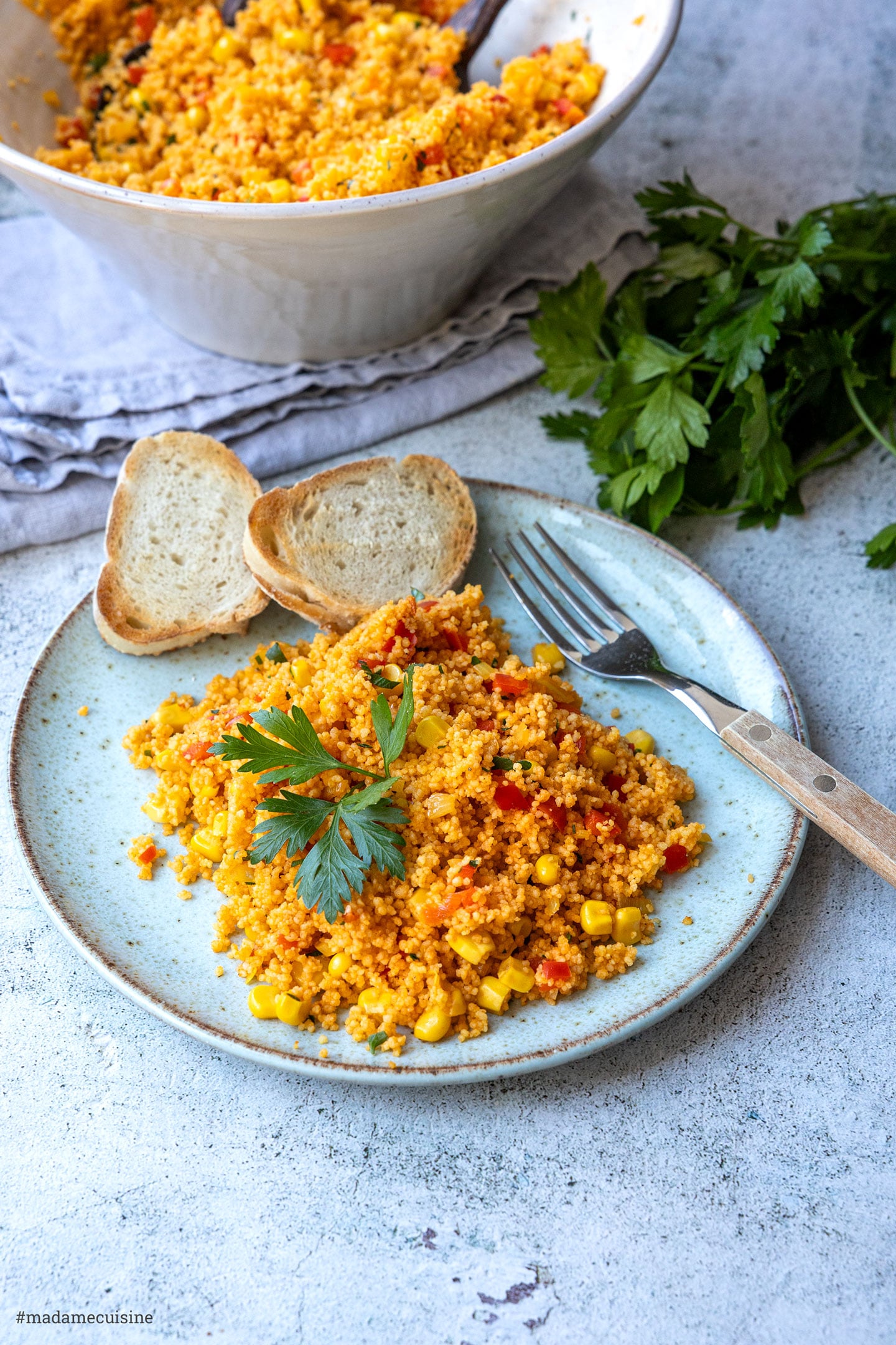 Paprika-Mais-Couscous auf einem Teller angerichtet, im Hintergrund die Salatschüssel und frische Petersilie