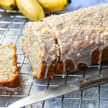 Angeschnittenes Bananenbrot mit Kokosguss und Bananen im Hintergrund