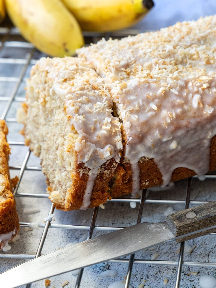 Angeschnittenes Bananenbrot mit Kokosguss und Bananen im Hintergrund