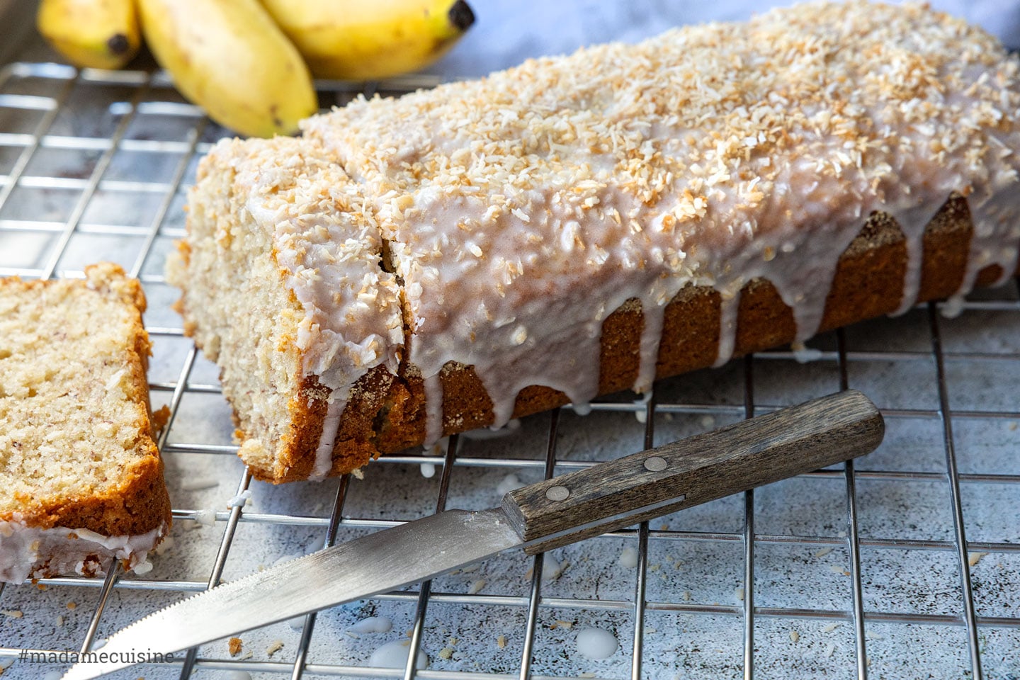 Kokos-Bananenbrot mit Zuckerguss und gerösteten Kokosraspeln, angeschnitten auf einem Kuchengitter