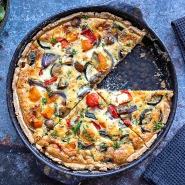 Herbstliche Quiche mit buntem Gemüse, ein Stück herausgeschnitten, in dunkler Backform