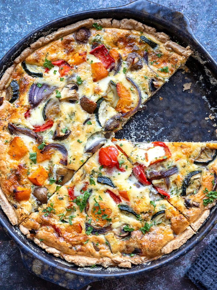 Herbstliche Quiche mit buntem Gemüse, ein Stück herausgeschnitten, in dunkler Backform