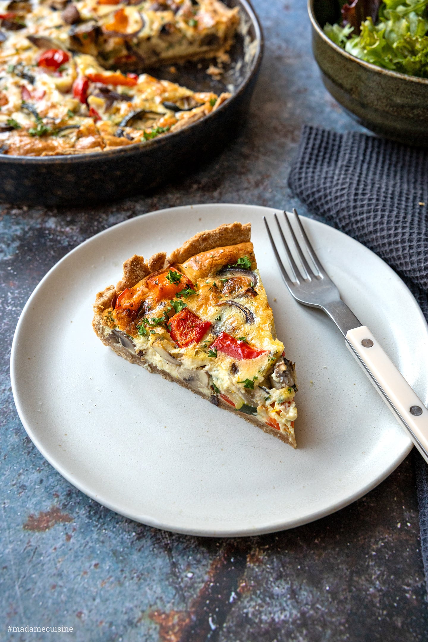 Stück Quiche mit knusprigem Vollkorn-Mürbeteig auf hellem Teller, Gabel daneben