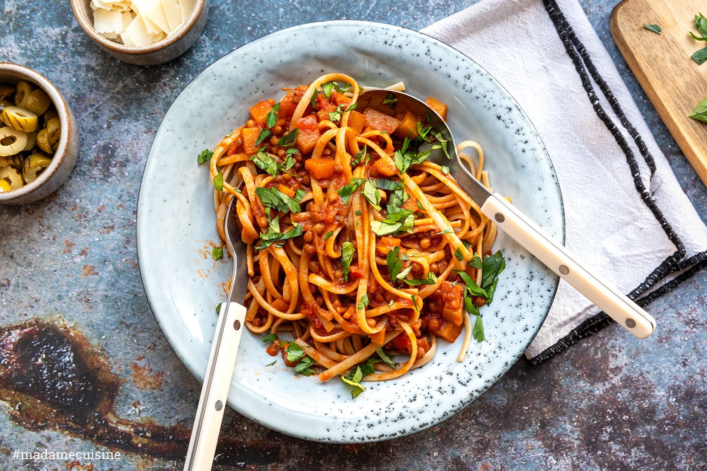 Kürbis-Linsen-Bolognese mit Vollkorn-Linguine in einem hellblauen Teller, garniert mit frischen Kräutern
