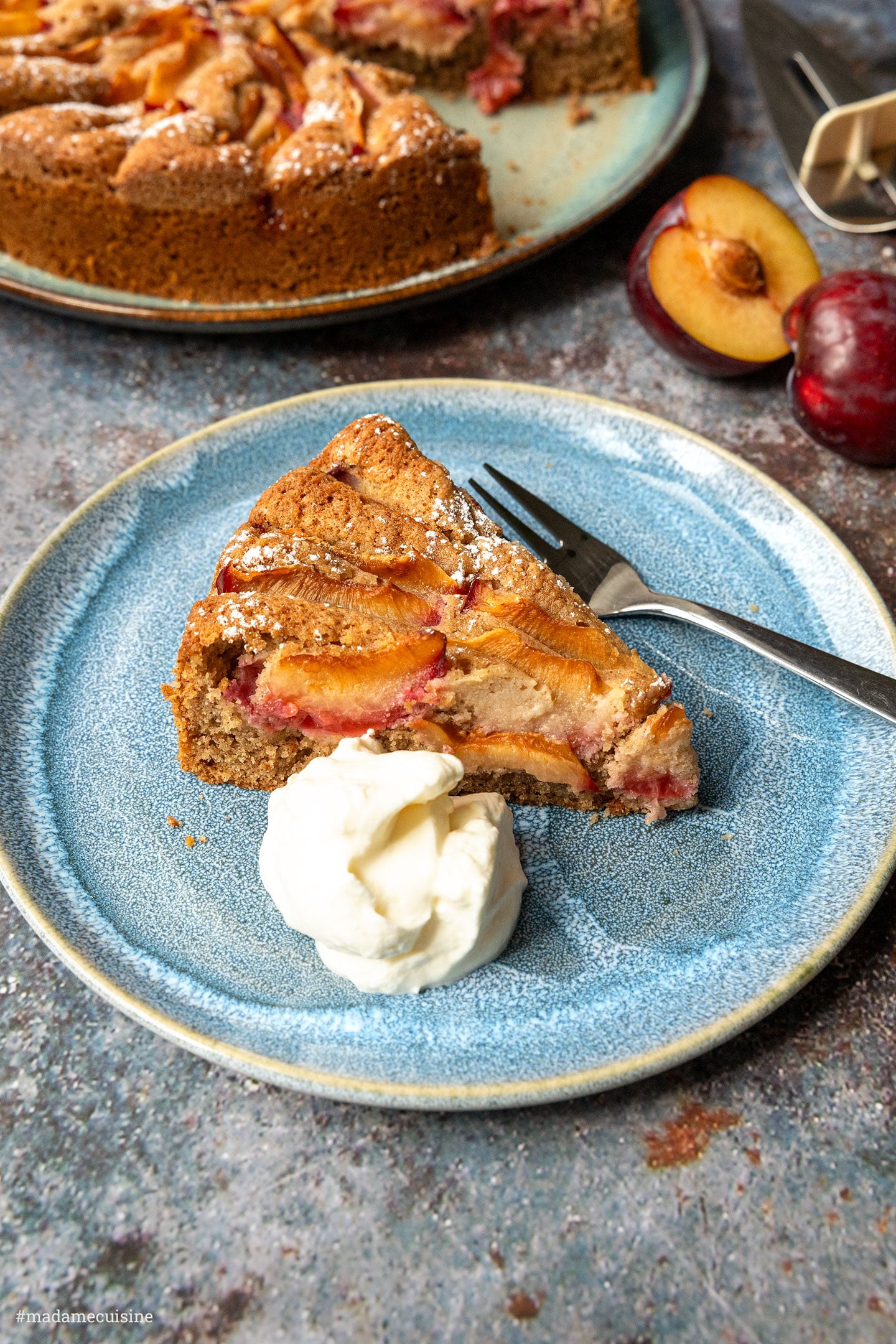 Pflaumenkuchen mit Buchweizenmehl, Kuchenstück mit einem Klecks Sahne