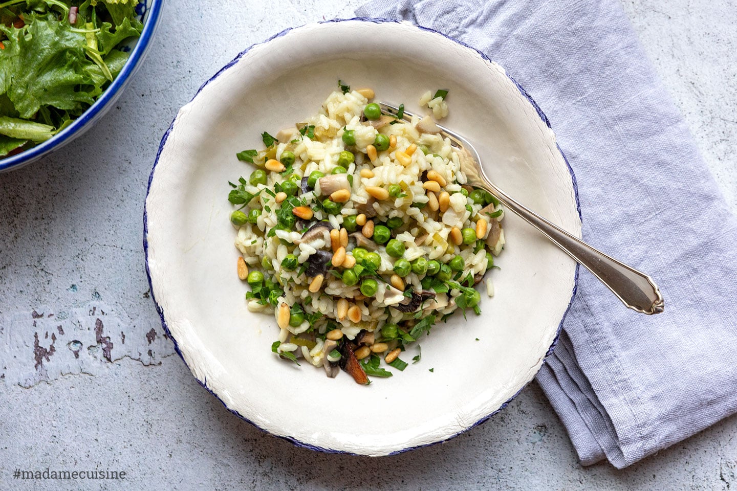 Risotto mit Austernpilzen und Erbsen auf blau berandetem Teller mit Gabel und grünem Salat