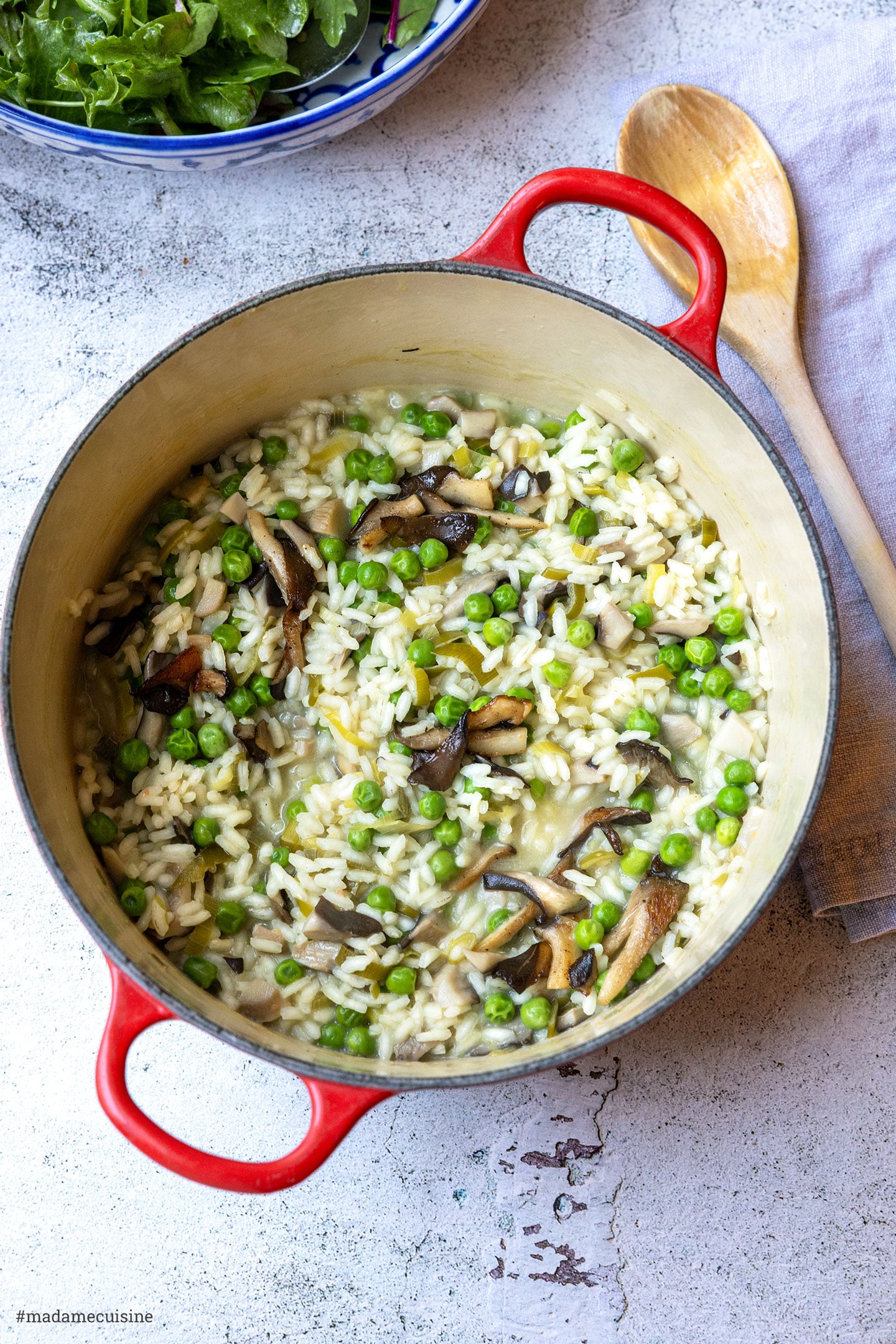 Risotto mit Austernpilzen und Erbsen im Topf, mit Kochlöffel und grünem Salat im Hintergrund