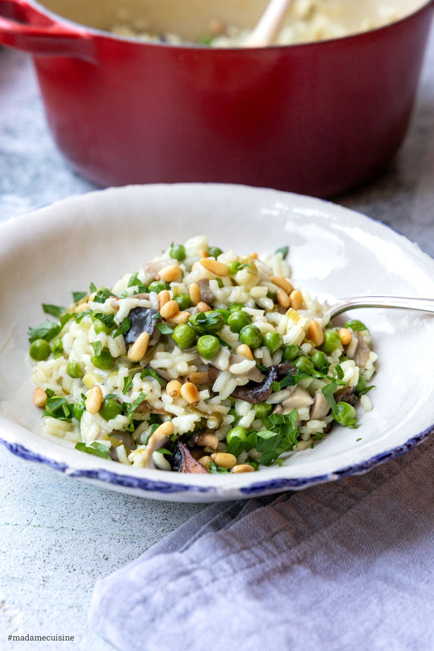 Risotto mit Austernpilzen und Erbsen, Löffel hebt eine Portion mit Erbsen und Pinienkernen an