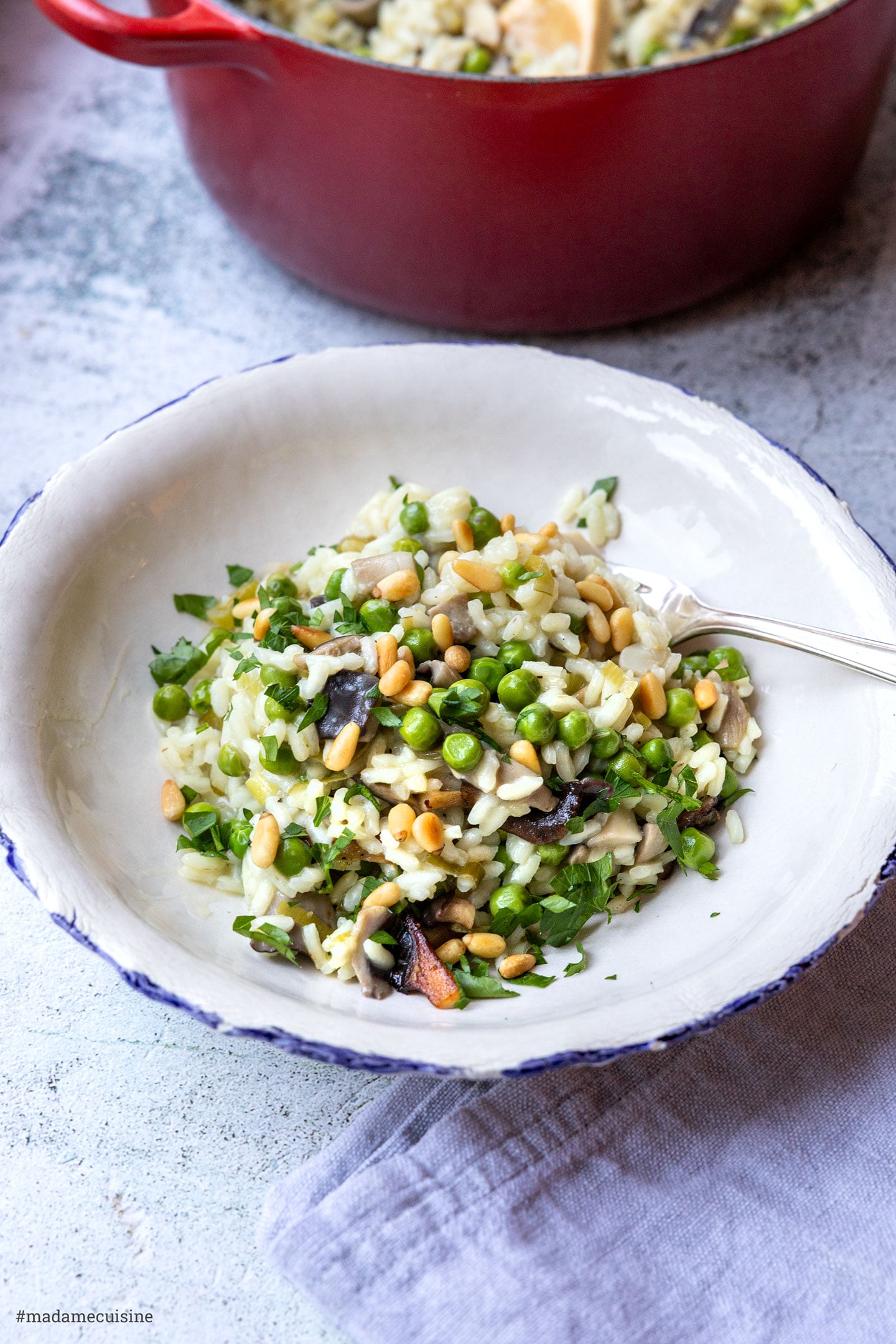 Portion Pilz-Erbsen-Risotto mit Pinienkernen und Petersilie auf Teller, Topf im Hintergrund