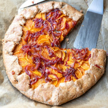 Angeschnittene Galette mit Süßkartoffeln und Zwiebel-Chutney auf Backpapier, daneben ein Tortenheber