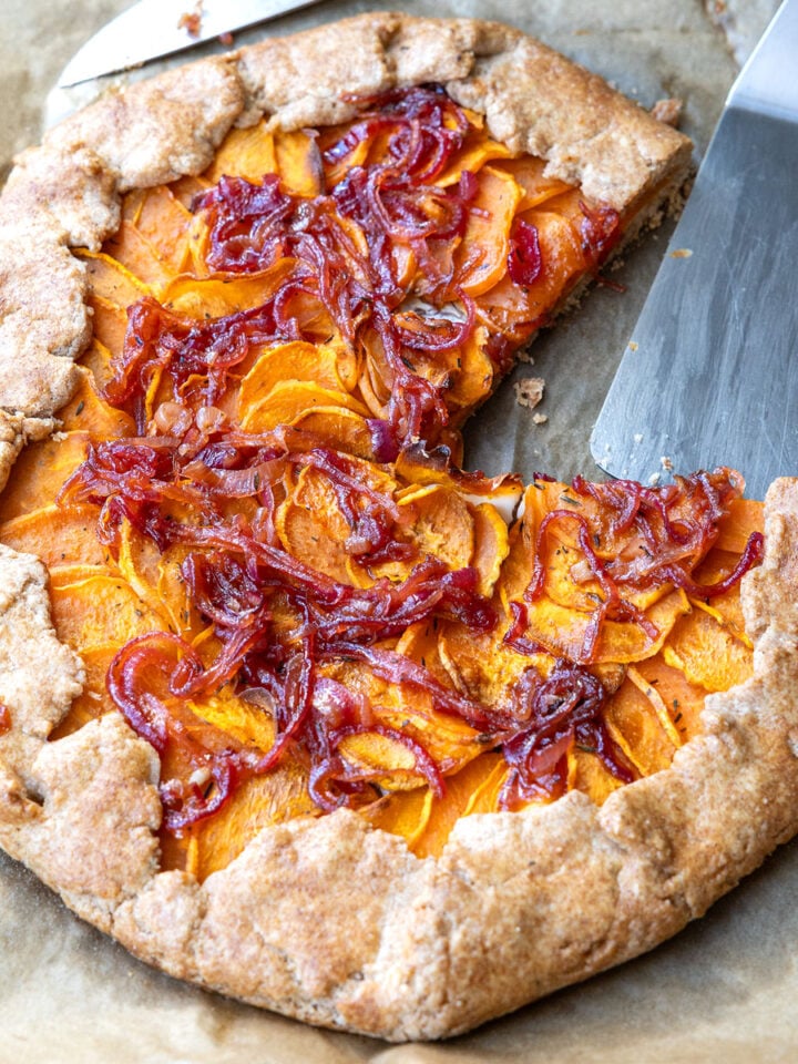 Angeschnittene Galette mit Süßkartoffeln und Zwiebel-Chutney auf Backpapier, daneben ein Tortenheber