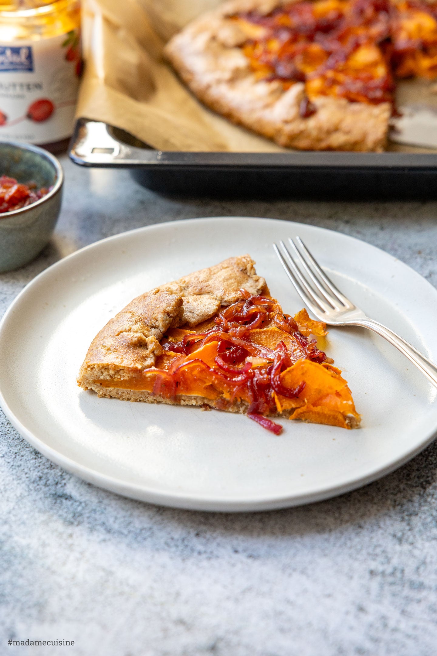 Stück Süßkartoffel-Galette von der Seite, die ganze Galette auf dem Blech im Hintergrund