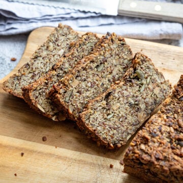 Hafer-Vollkornbrot in dicken Scheiben auf einem Holzbrett, daneben ein Brotmesser