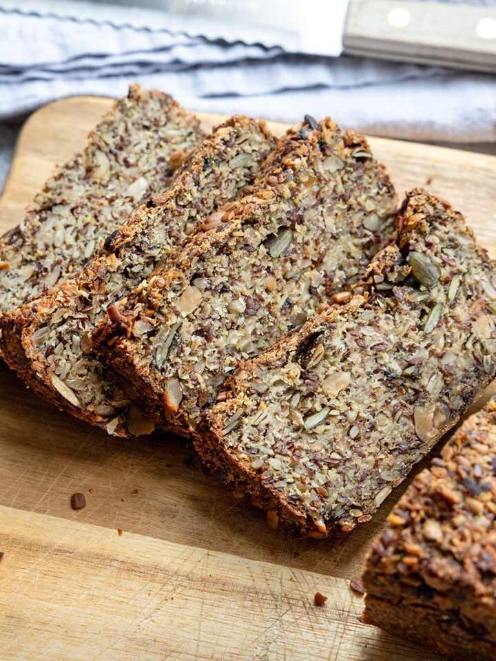 Hafer-Vollkornbrot in dicken Scheiben auf einem Holzbrett, daneben ein Brotmesser