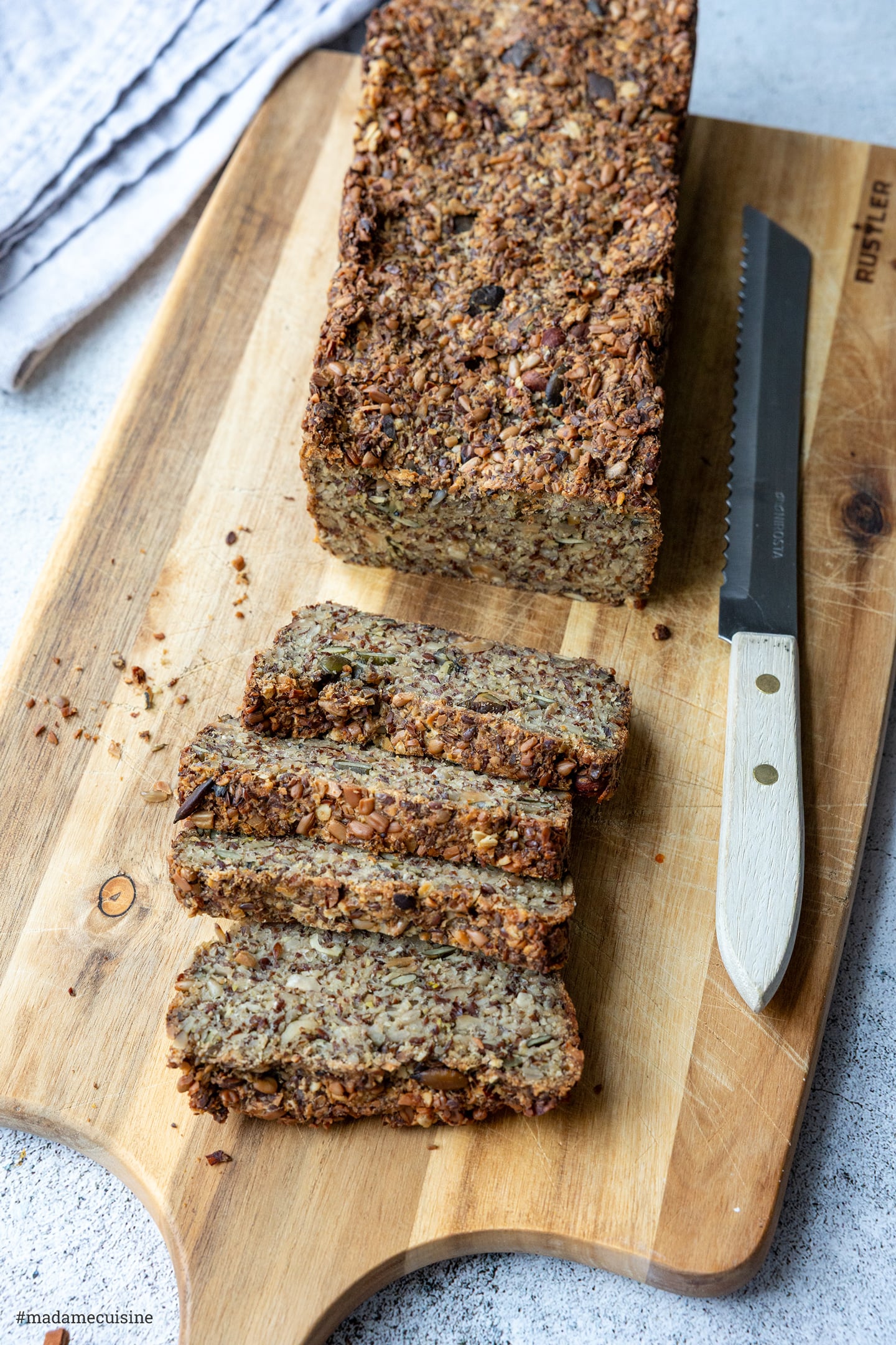 Körnerbrot mit knuspriger Kruste, davor vier Scheiben auf einem Holzbrett