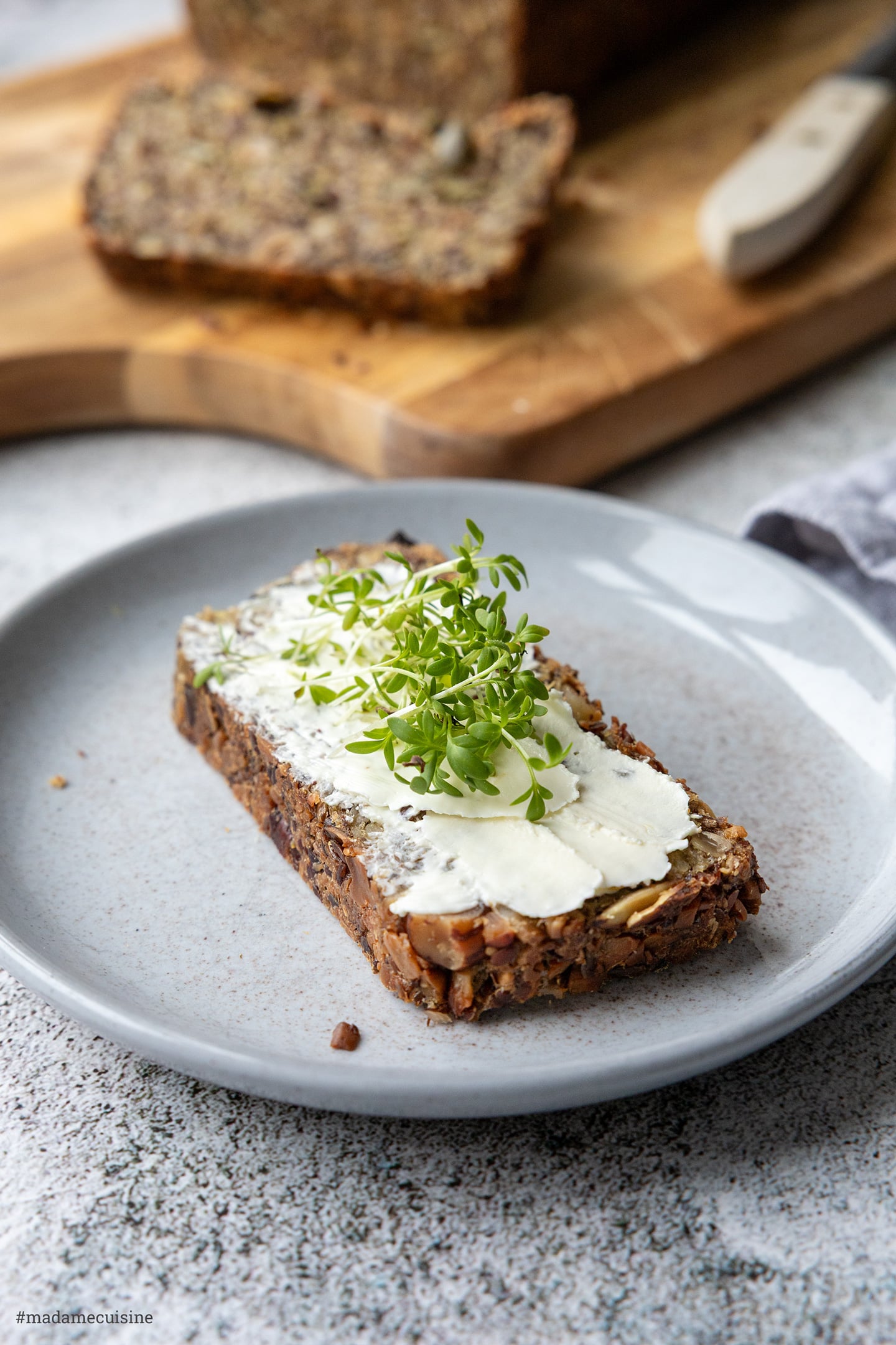 Scheibe Hafer-Vollkornbrot mit Frischkäse und Kresse auf einem grauen Teller