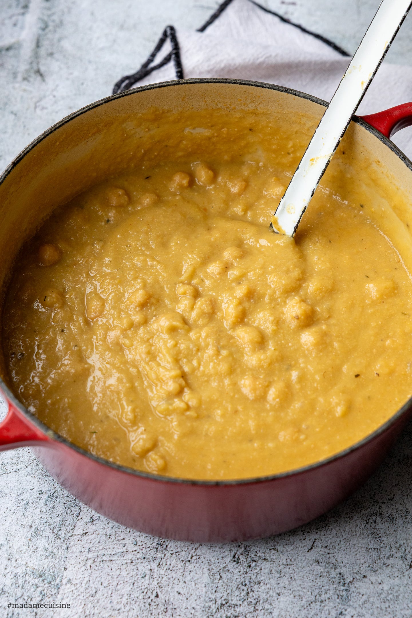Cremige Kichererbsensuppe im roten Gusseisentopf mit Kelle