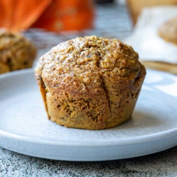 Saftige Kürbis-Muffins auf einem hellgrauen Teller, im Hintergrund Hokkaido-Kürbisse