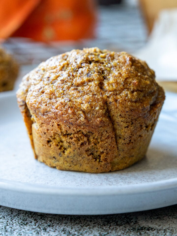 Saftige Kürbis-Muffins auf einem hellgrauen Teller, im Hintergrund Hokkaido-Kürbisse