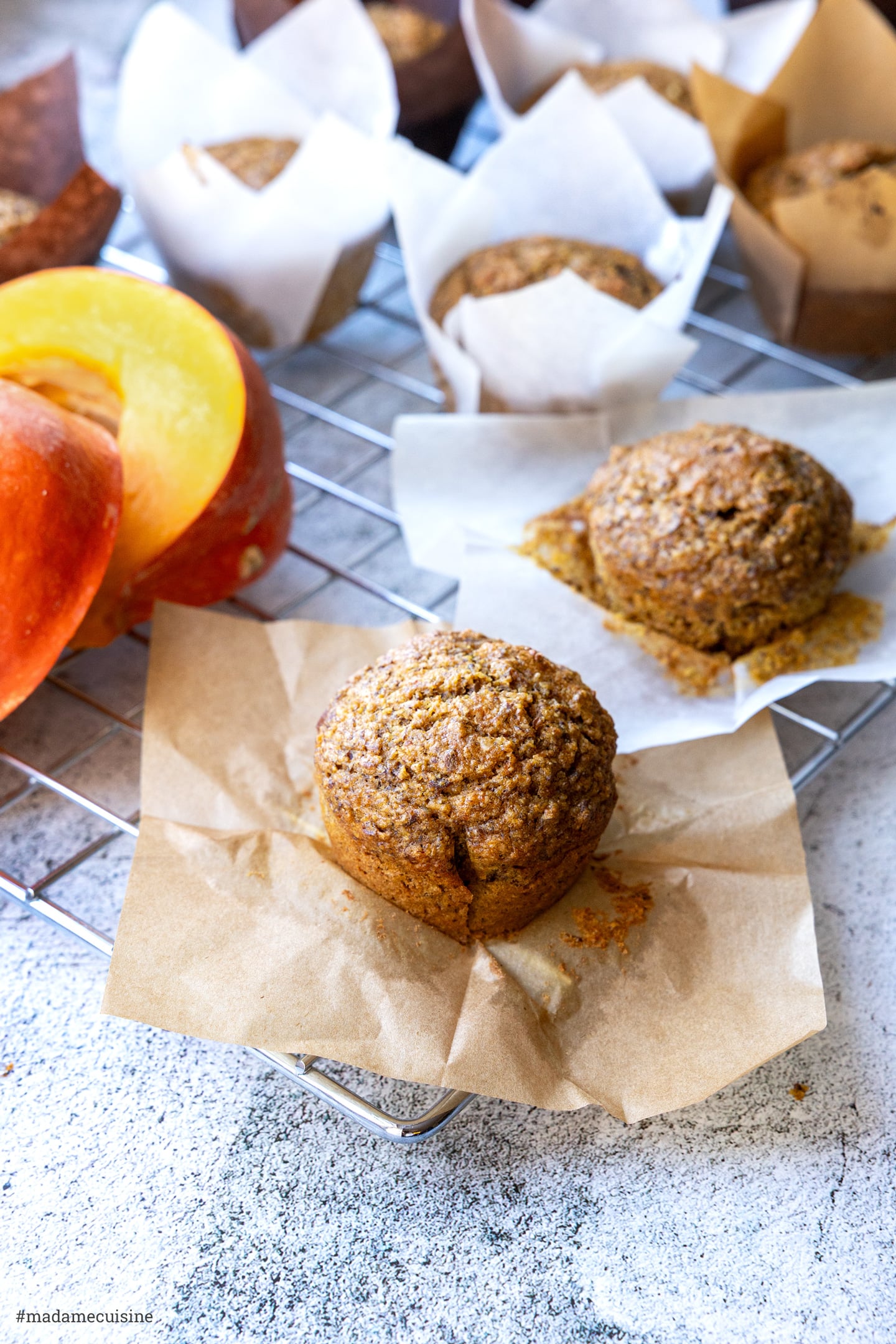 Muffins in Papierförmchen auf einem Kuchengitter neben einem halbierten Hokkaido-Kürbis