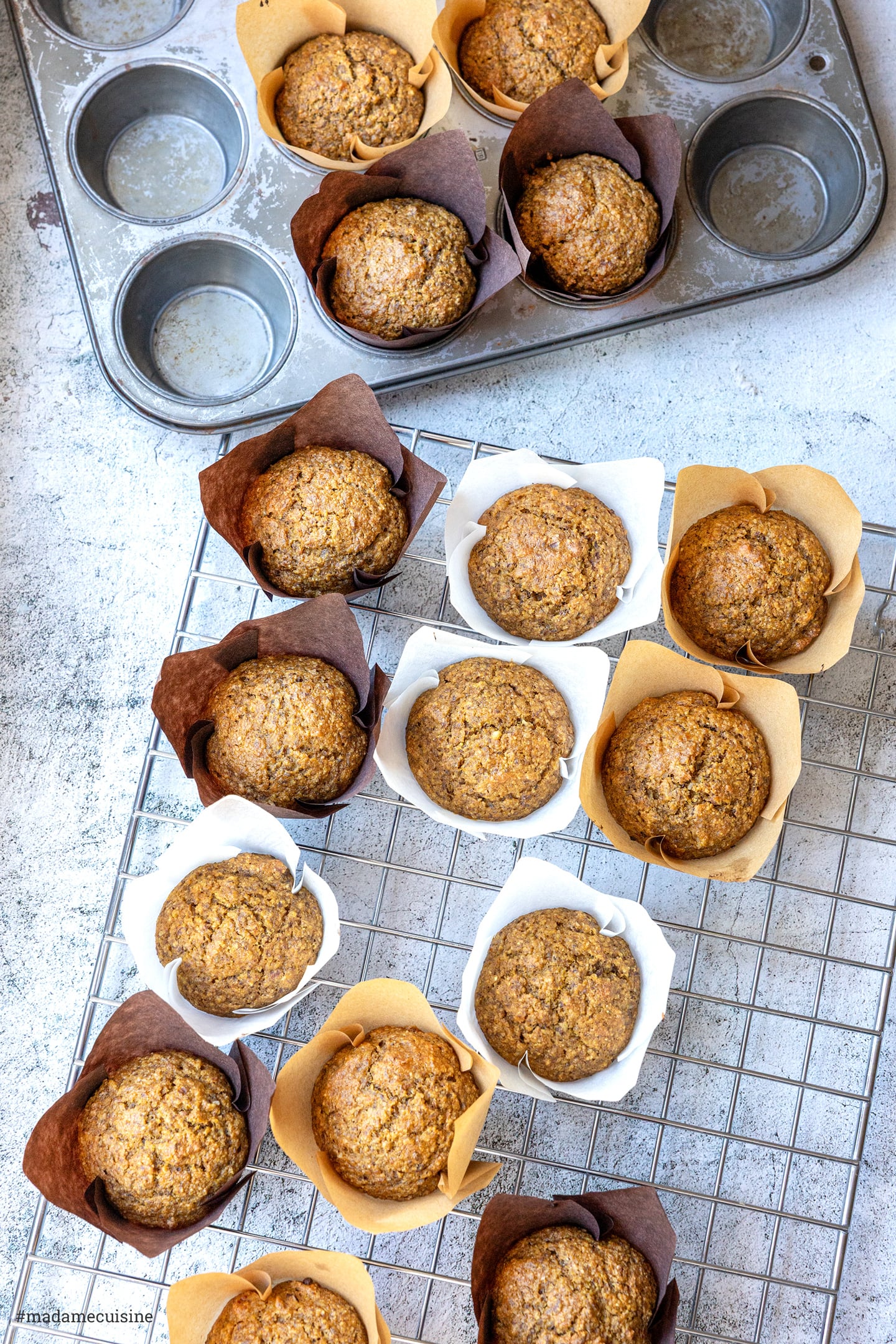 Kürbis-Muffins in braunen, weißen und naturfarbenen Tulpenförmchen auf dem Kuchengitter, von oben