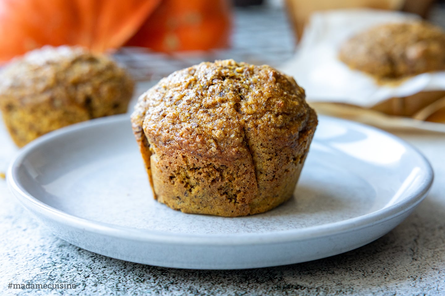 Saftige Kürbis-Muffins auf einem hellgrauen Teller, im Hintergrund Hokkaido-Kürbisse