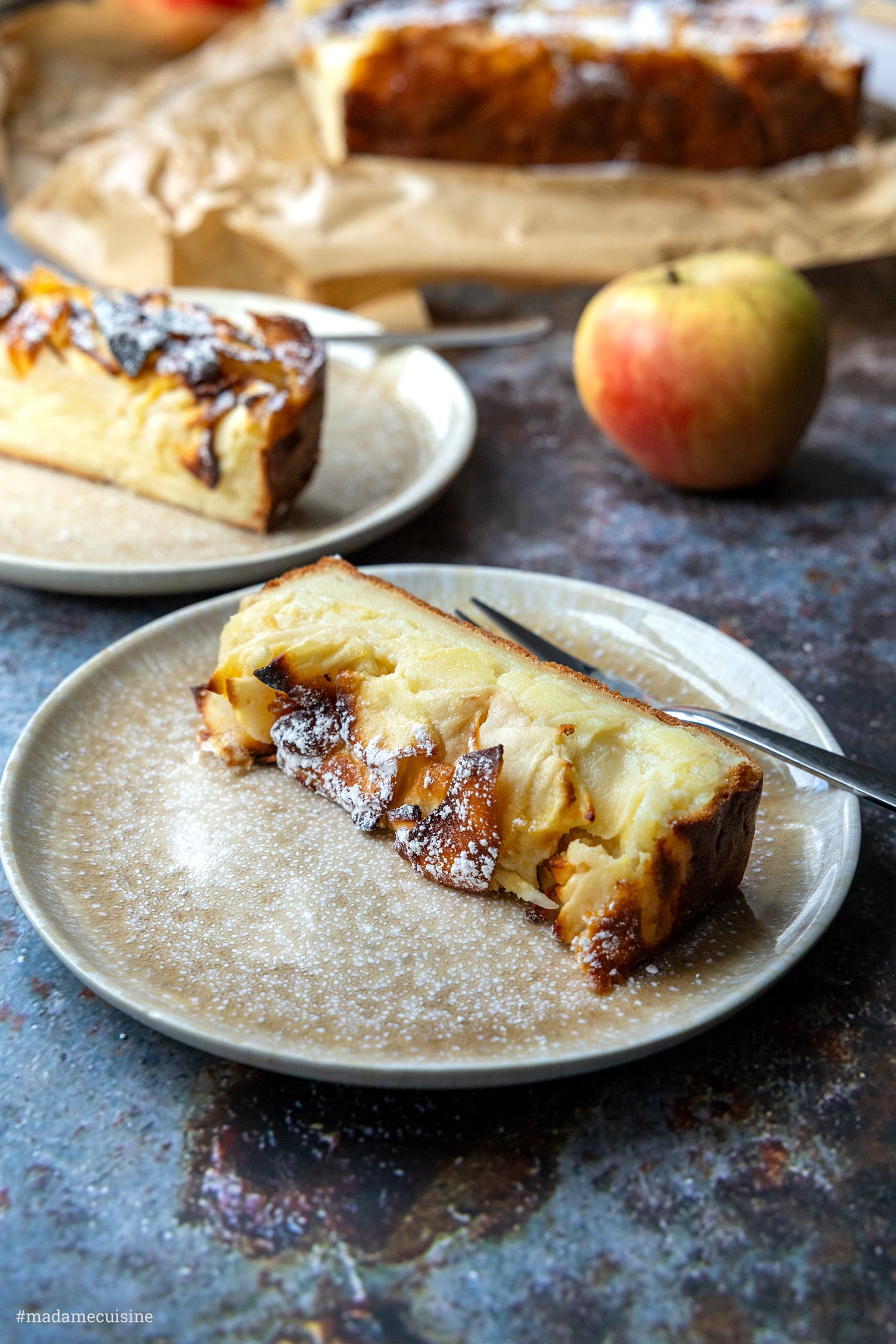 Zwei Stücke Apfelkuchen mit hauchdünnen Apfelscheiben, angeschnittener Kuchen im Hintergrund
