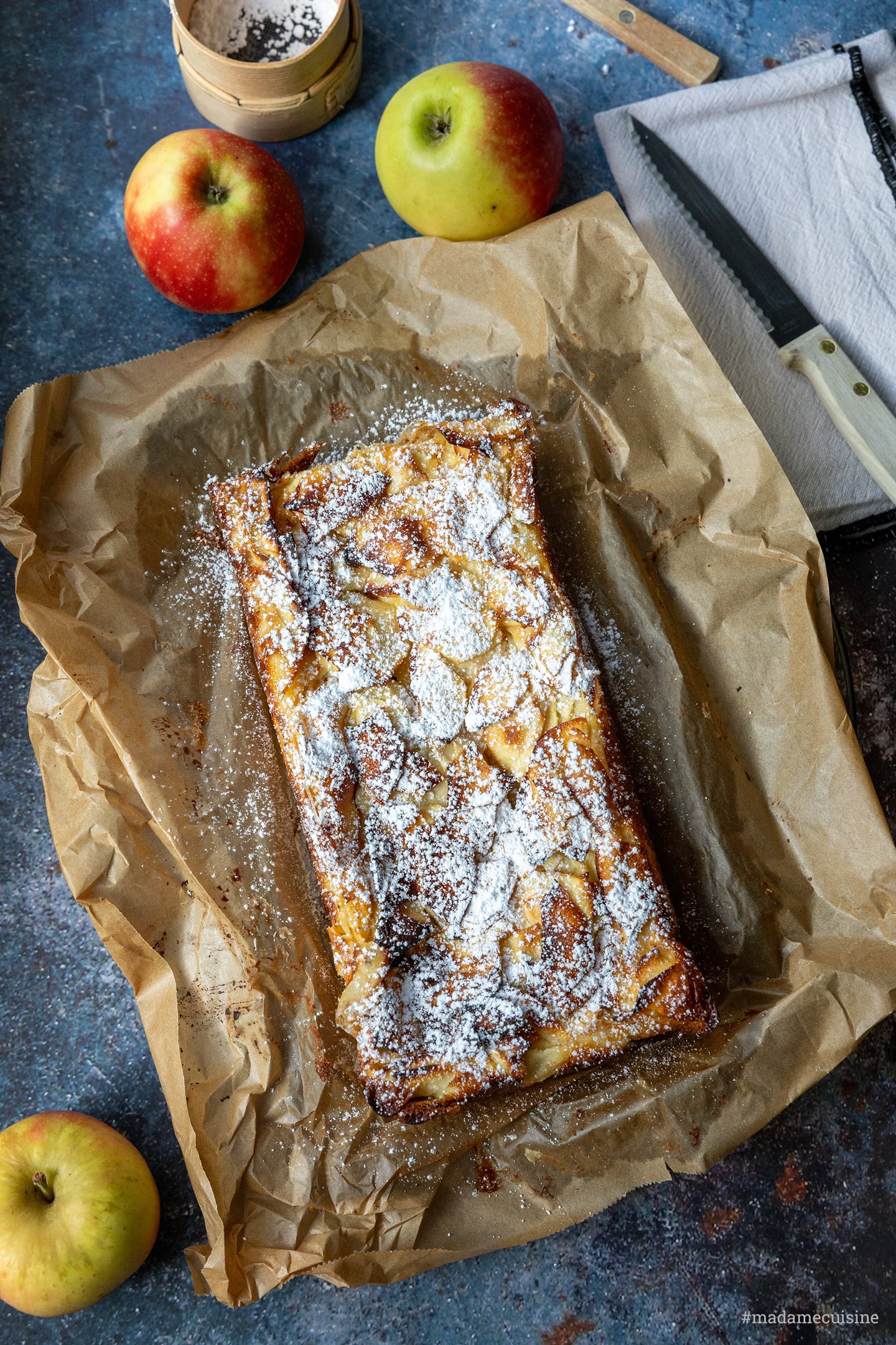 Unsichtbarer Apfelkuchen aus der Kastenform von oben auf Backpapier, daneben Äpfel und Messer